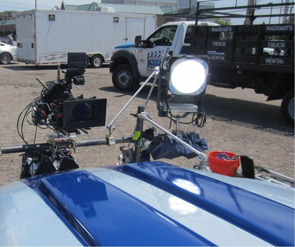 Film set camera rig and lighting equipment attached to a production vehicle for movie staging
